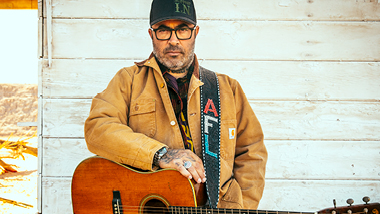 Aaron Lewis with his guitar in front of a house.