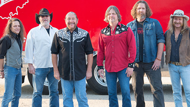 The Marshall Tucker Band stands in front of a red tour bus.