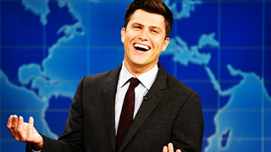 Colin Jost laughing while sitting at the Weekly Update desk