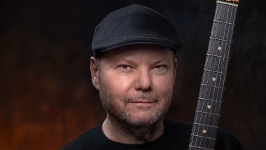 Christopher Cross with brown background holding guitar
