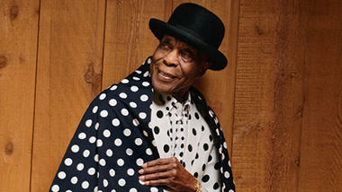 Buddy Guy in black and white suit with wooden background